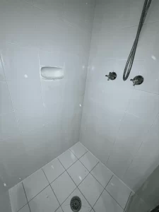 White floor and wall tiles in shower in desperate need of new grout.