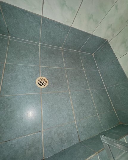 Shower base before regrouting showing stained and deteriorated grout in a Perth bathroom