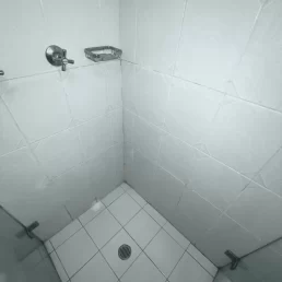 A shower with white floor and wall tiles with old dirty and mouldy stained grout.